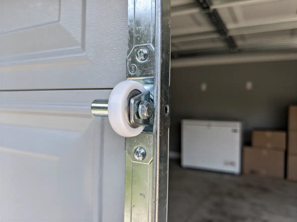 A white garage door roller is attached to a metal track.